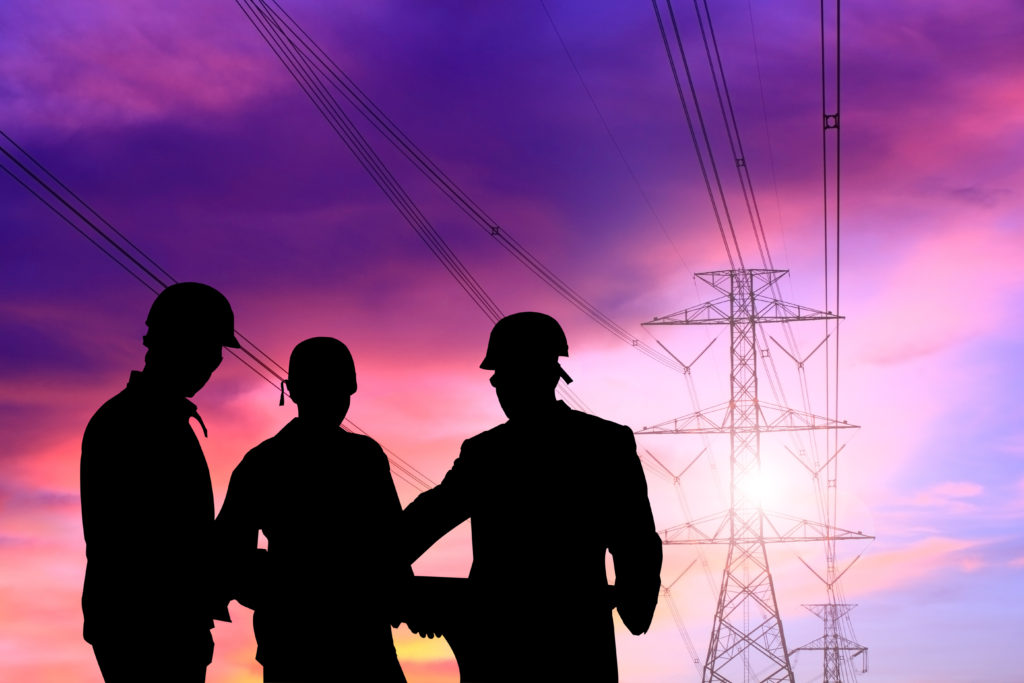 black silhouettes of electrical contractors near power lines at sunset