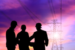 black silhouettes of electrical contractors near power lines at sunset