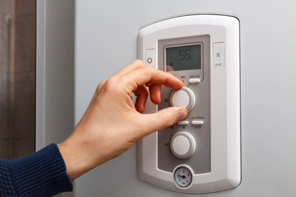 Men hand regulate temperature on 55 degree in control panel of central heating and cooling unit