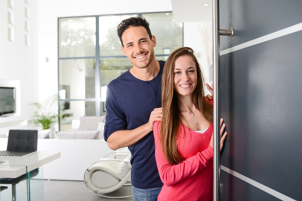 happy young couple at new house front door welcoming people