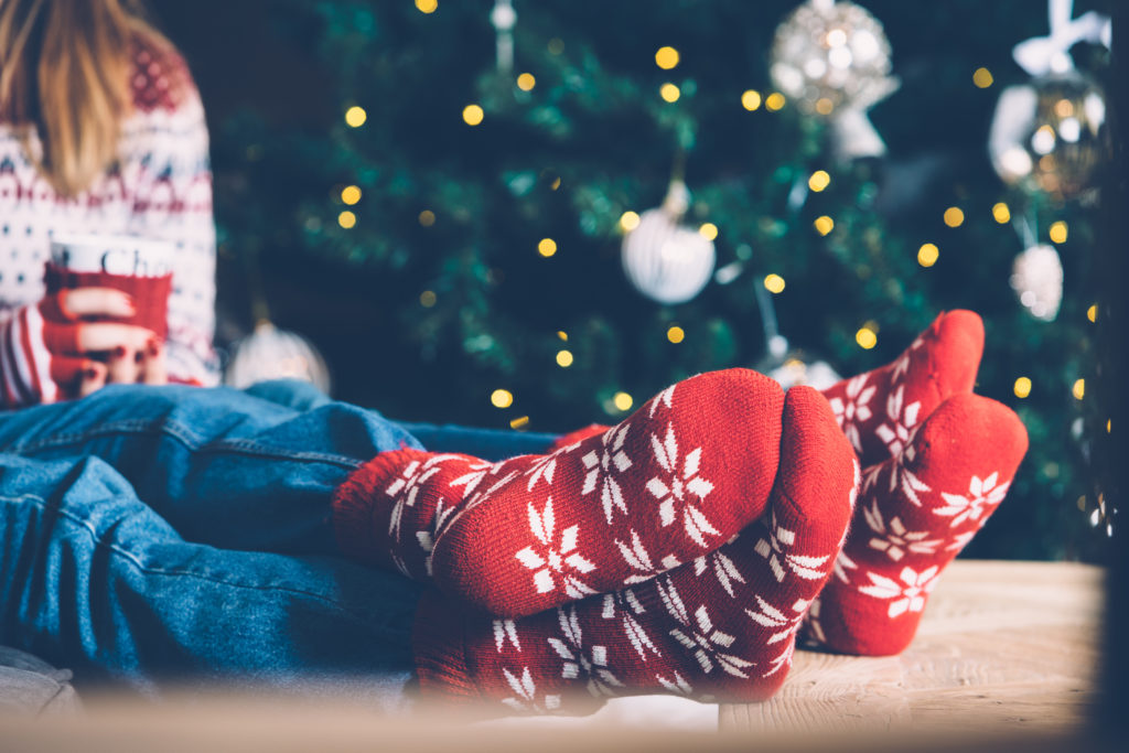 Crop shot of people's feet in red-and-white socks sitting together against Christmas-tree.