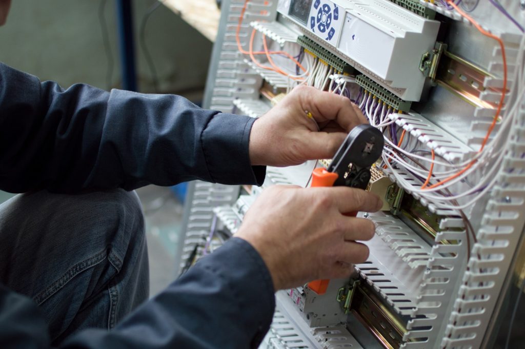 Electrician assembling industrial control cubicle in workshop. Close-up photo.