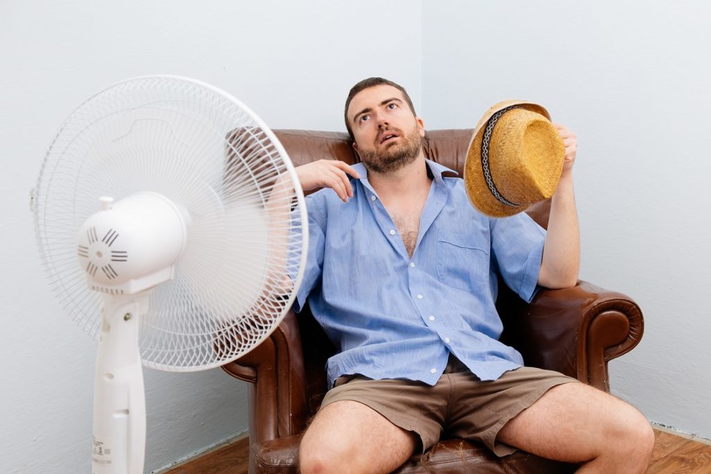 Flushed man feeling hot in front of a fan