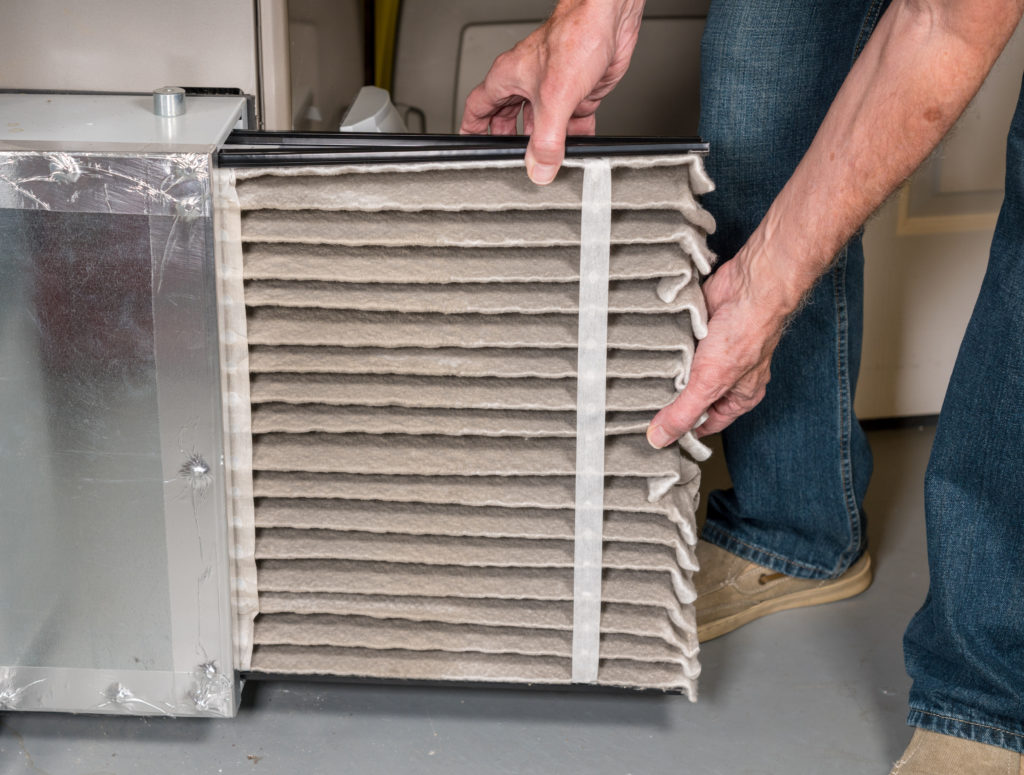 Senior caucasian man changing a folded dirty air filter in the HVAC furnace system in basement of home