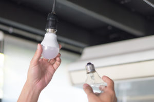 A person switching out an old incandescent bulb with a new LED bulb