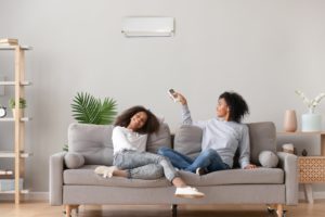 Happy african family relax on sofa under air conditioner, black mom holding remote control switch on conditioning in living room adjust comfort temperature for daughter, climate system at modern home