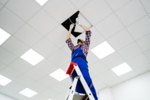 Electrician On Stepladder Installs Lighting To The Ceiling