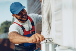 A happy AC repairman performing air conditioning repairs on an exterior HVAC unit.