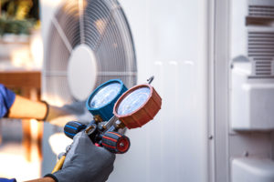 A person holding red and blue gauges while performing HVAC maintenance in El Paso.