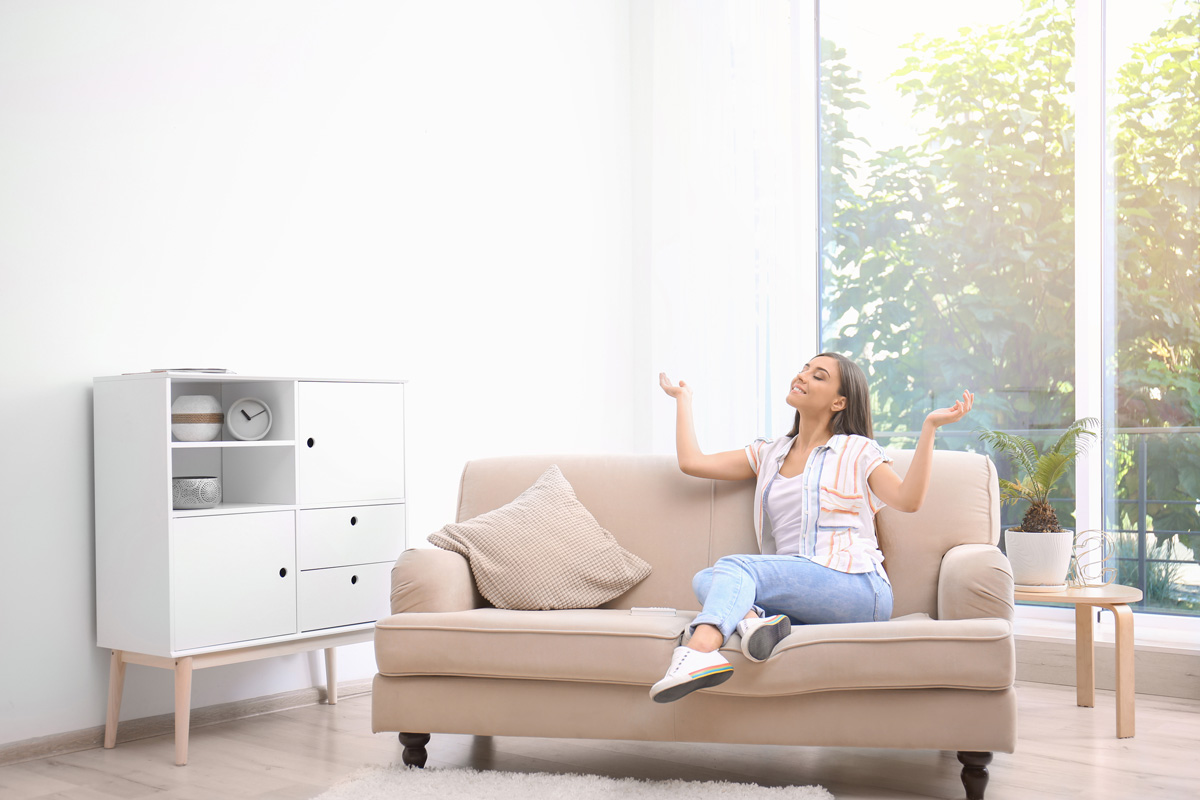 A woman sitting on a couch smiling while feeling refrigerated air in El Paso.