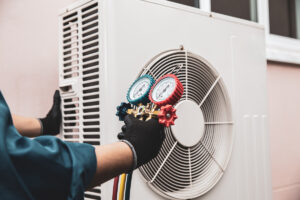 A person wearing black gloves holding a pressure gauge while performing maintenance on an HVAC system in El Paso.