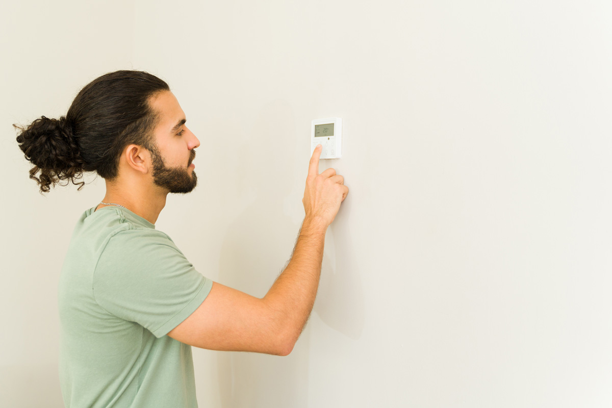 A person in a green shirt adjusting a wall thermostat in El Paso.
