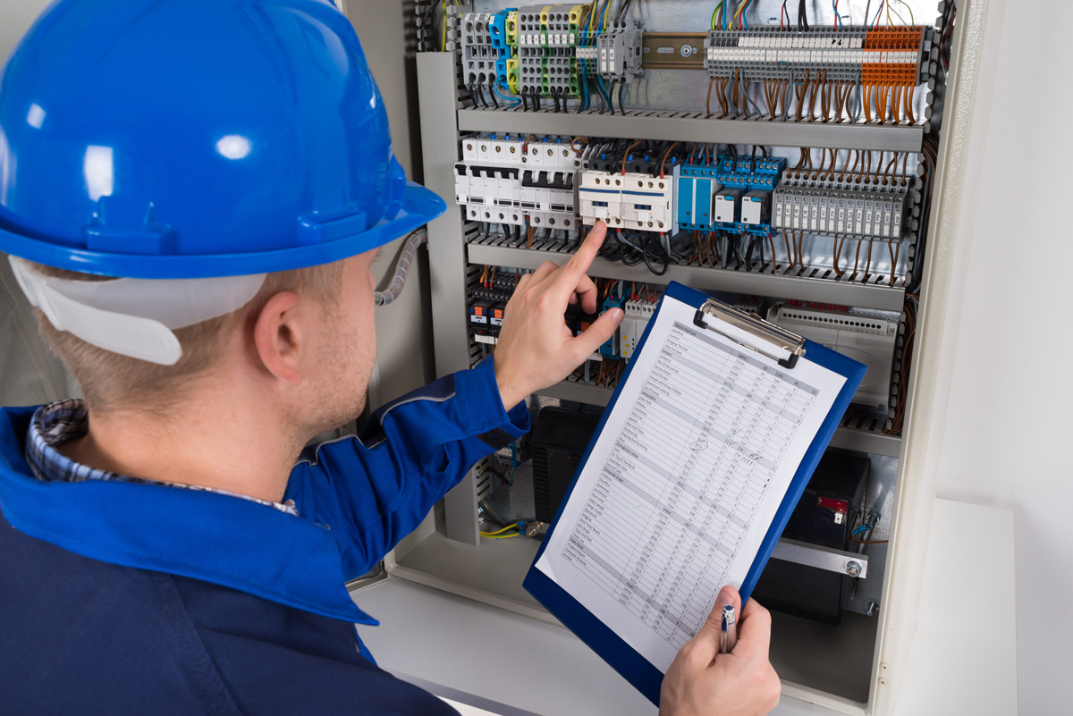 A person with a blue hard hat holding a checklist while looking at an electrical box in El Paso.